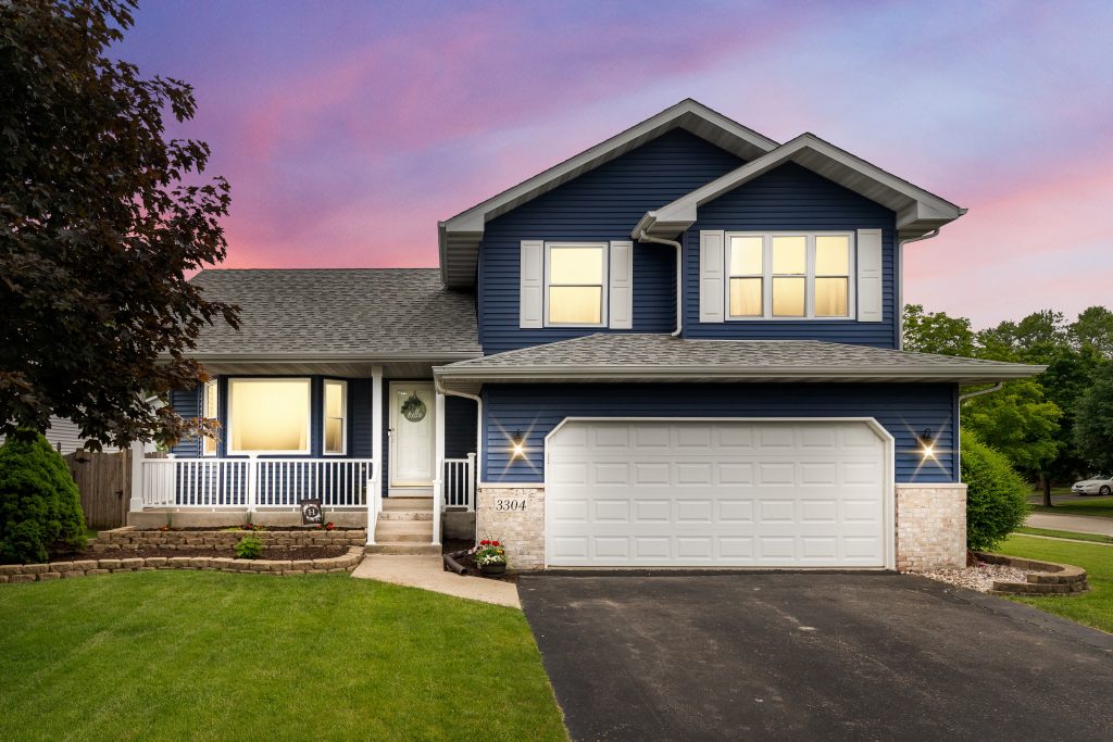 exterior of a suburban home with blue siding a white front porch and white shutters at sunset