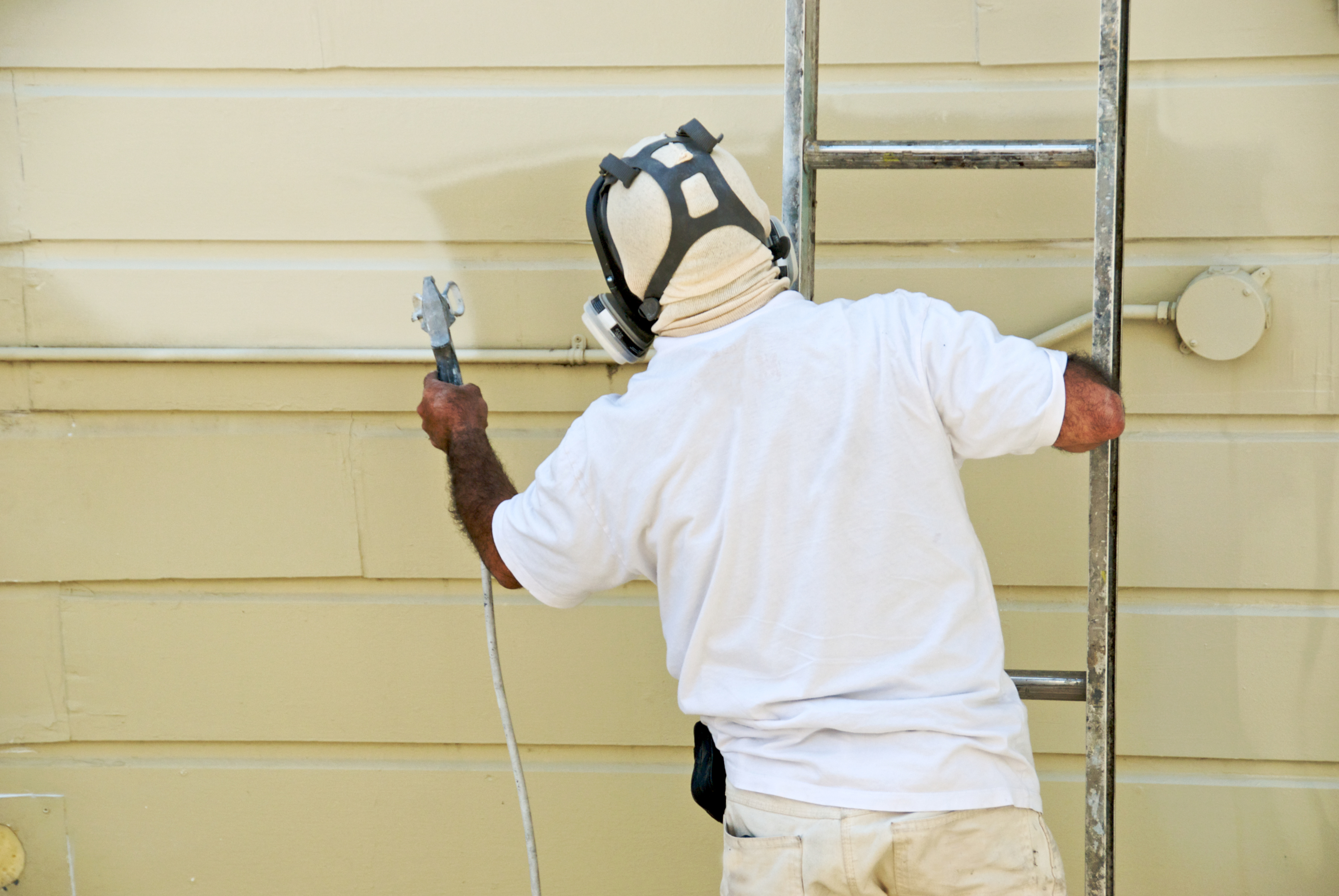 A person painting Hardie Board siding with a sprayer