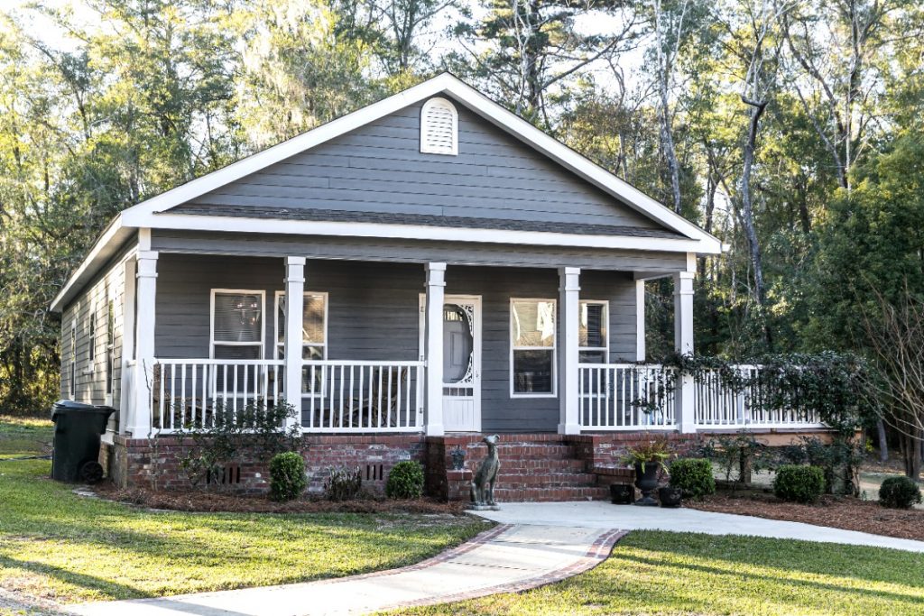 Small blue gray mobile home with a front and side porch with white railing