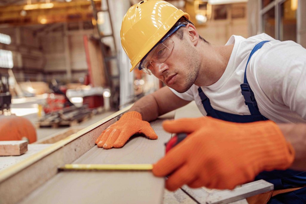 Serious man builder measuring wooden plank at construction site