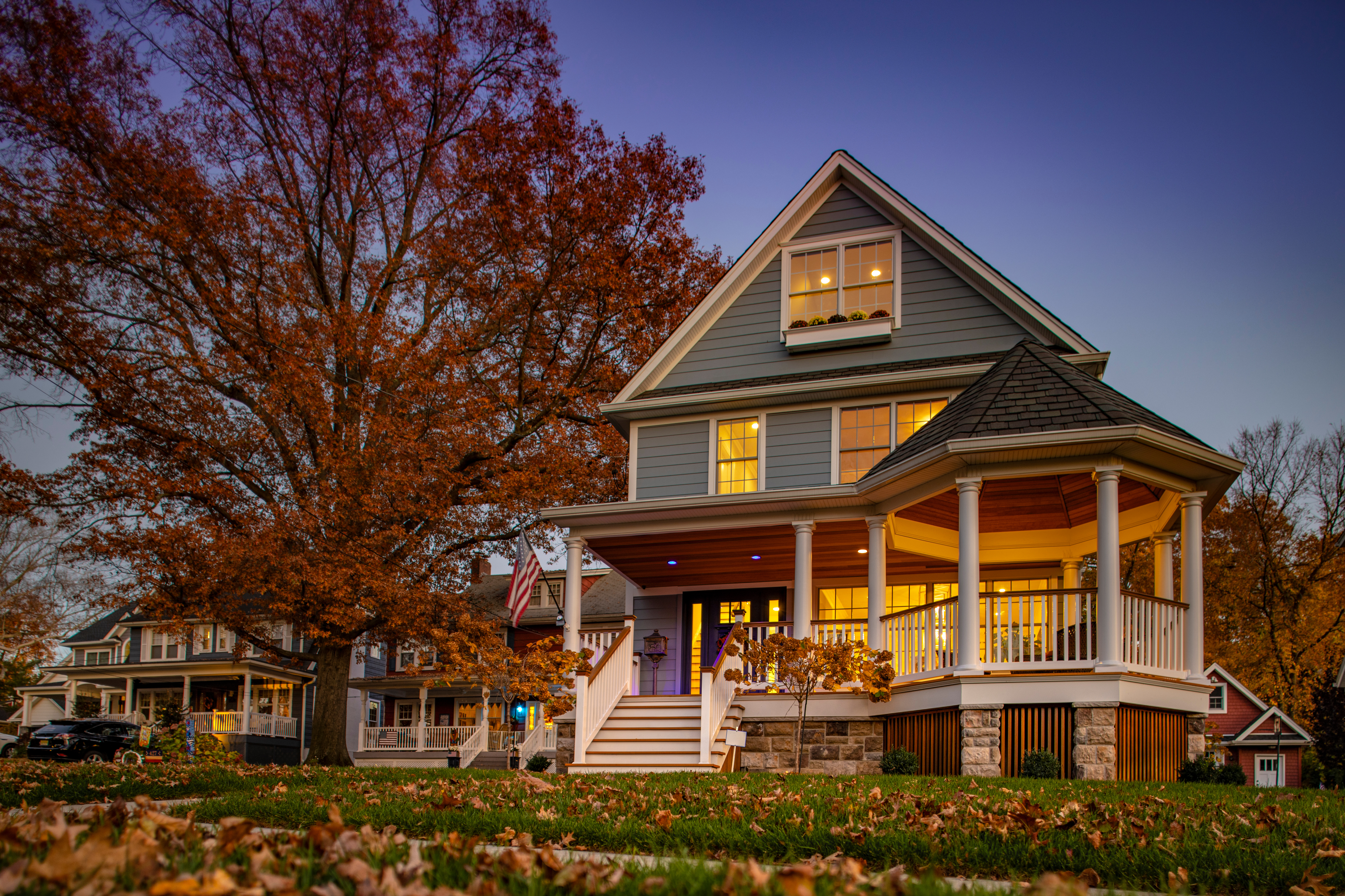 Low angle residential home photographed at twilight with autumn foliage on trees and ground