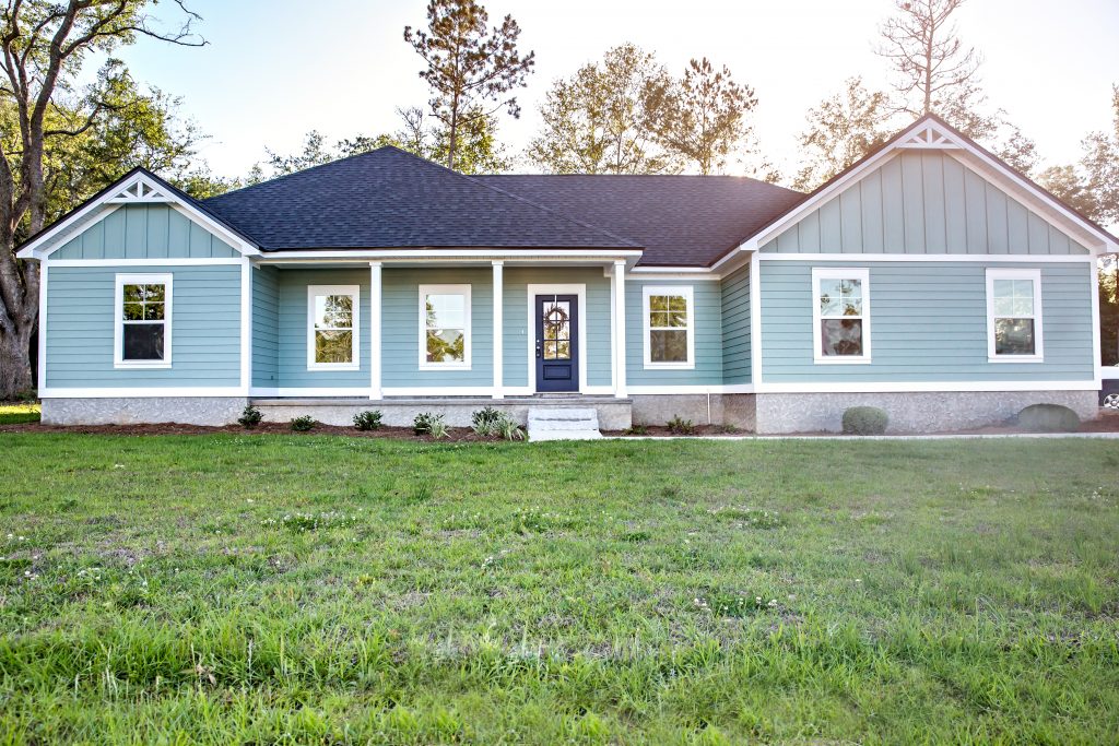 Front view of a brand new construction house with blue siding, a ranch style home with a yard