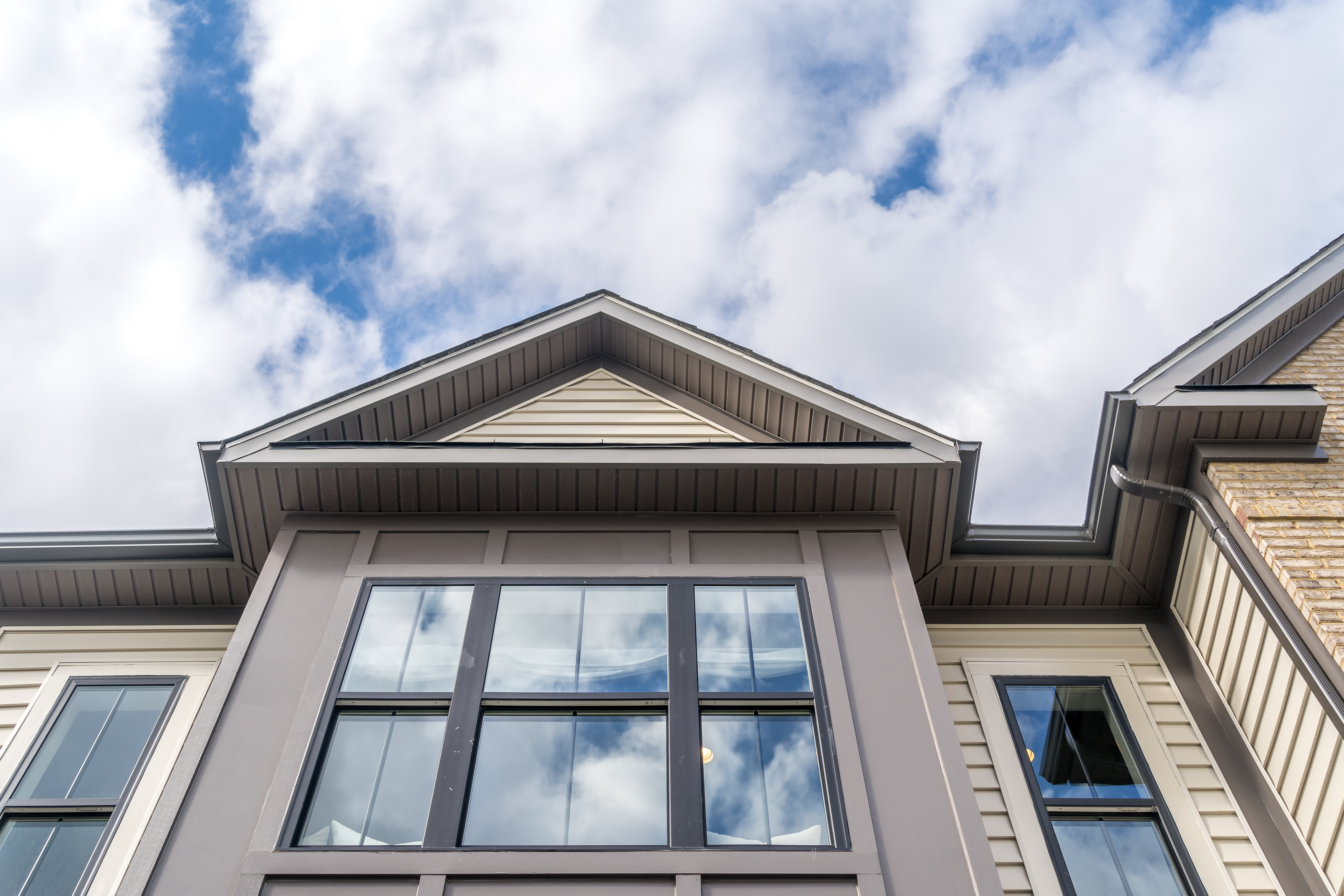 Cloudy sky reflecting on a newly installed window with dark brown aluminum frame and grills on an American single family house