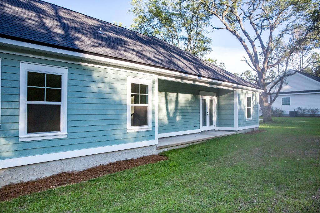 rear view of a brand new construction house with blue siding, a ranch style home with a yard on a sunny day